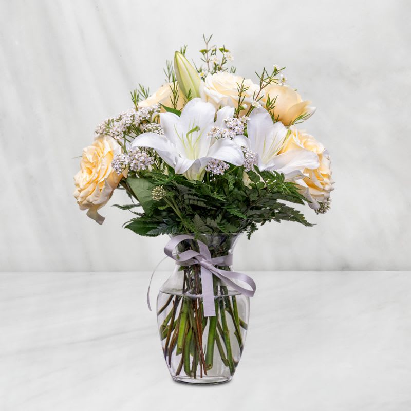 Bouquet of white lilies and pale peach roses in a glass vase