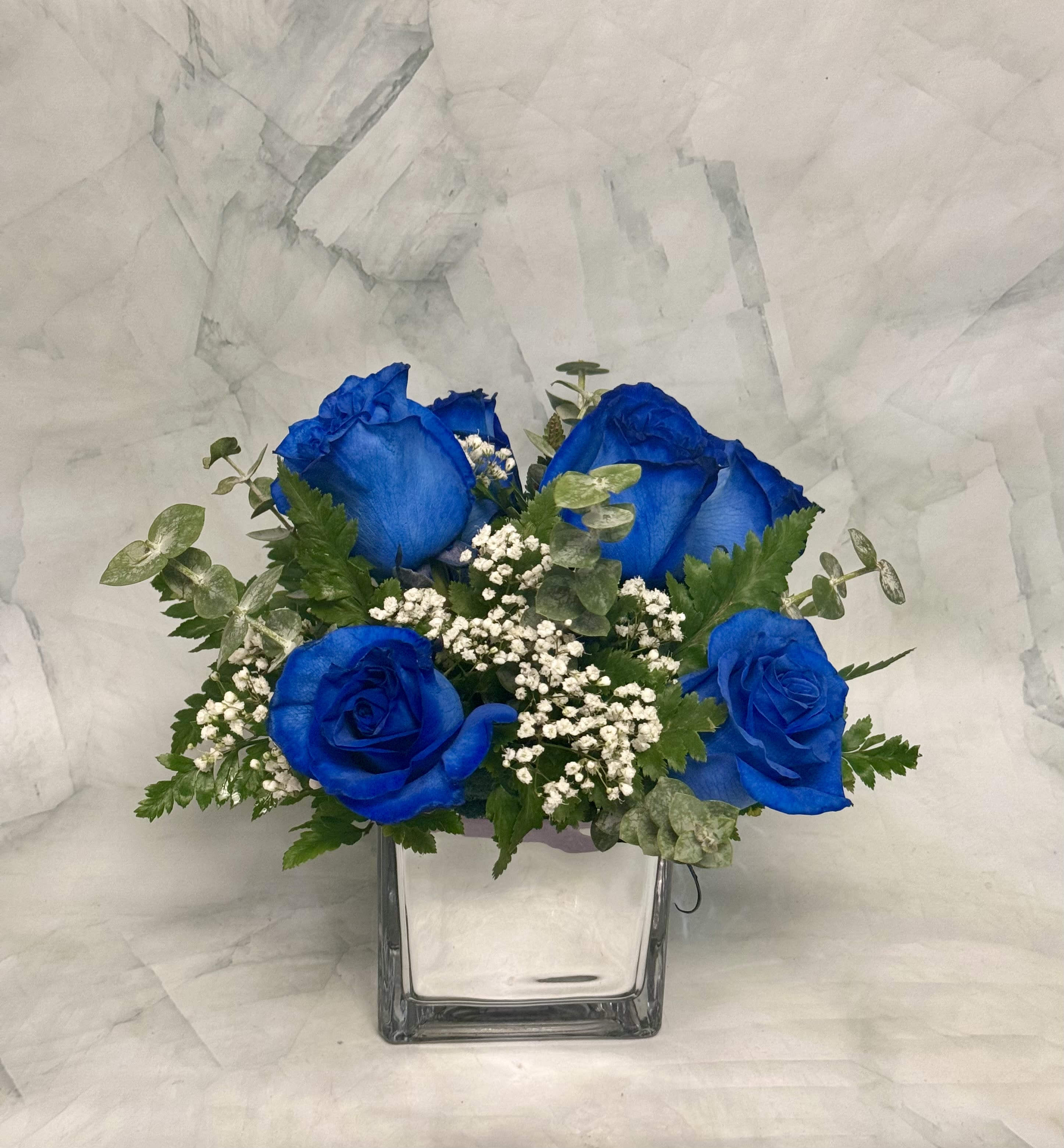 Blue roses in a clear square vase with baby's breath