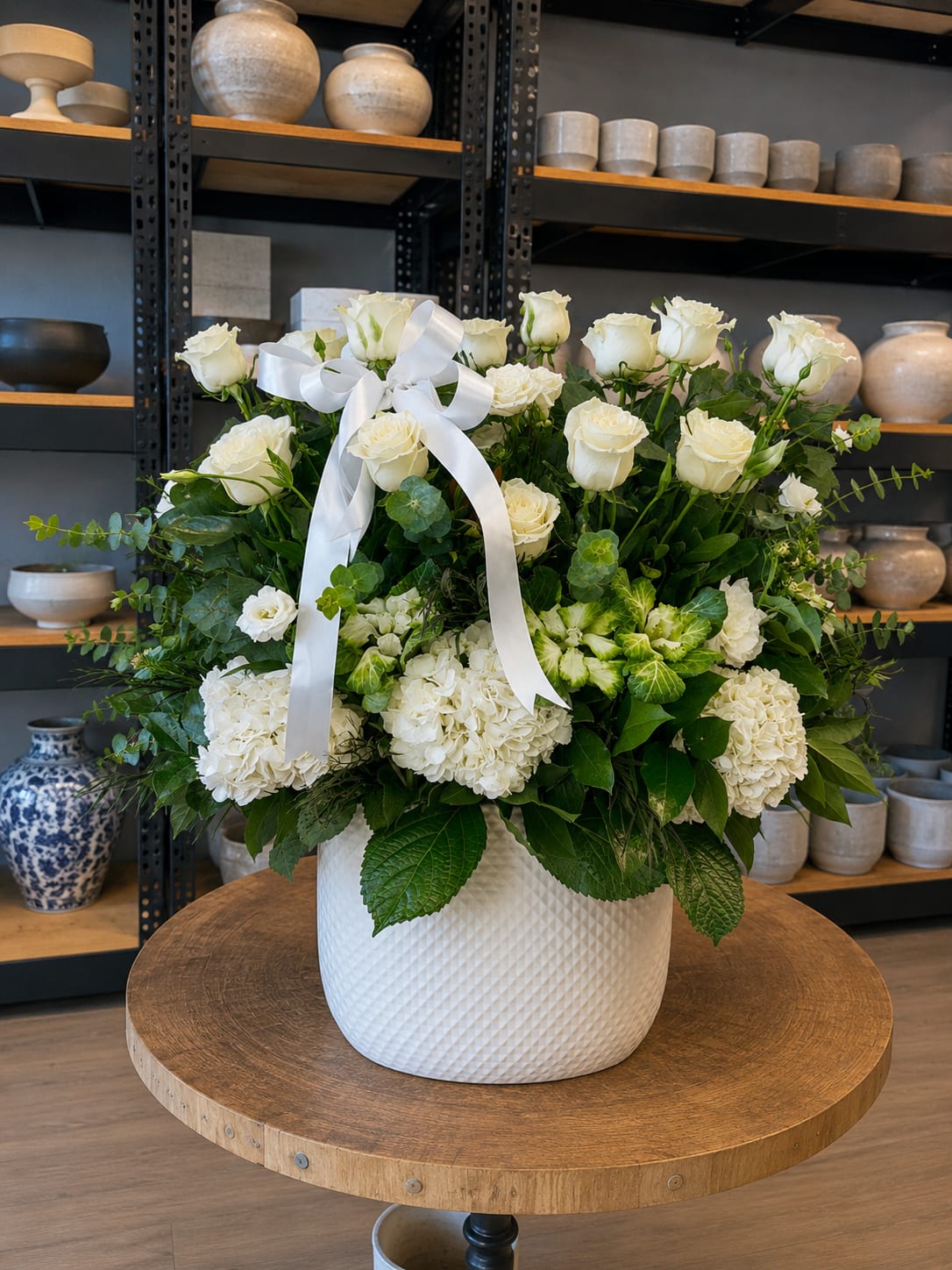 White roses and hydrangeas in a white vase with a ribbon