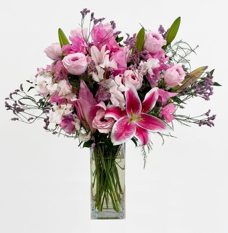 Noir Elegance by The Flower Spot™ - A lush rounded bouquet built around a show-stopping magenta stargazer lily gives this flower arrangement a romantic, luxurious feel-ideal as an anniversary bouquet or celebratory gift for someone you want to make feel truly seen. Noir Elegance by The Flower Spot™ blends lilies, premium roses and delicate sweet peas in a feminine palette of pink, white, purple and fresh greenery so the recipient experiences layers of color and texture the moment it's set in their room.  Soft pink roses and pale lilies nestle with airy purple filler blooms and a touch of green for depth, while a prominent magenta stargazer lily anchors the front for dramatic flair. The stems sit in a clear rectangular glass vase that keeps the presentation clean and modern and showcases the long, elegant stems. Each stem is hand-curated by our designer to create a full, rounded silhouette that reads lush from every angle.  Perfect for romantic occasions, birthdays, or to celebrate a milestone, this arrangement sends a message of thoughtful luxury and warmth-she'll feel celebrated and cherished. Vase included; to keep flowers fresh, change the water every 2-3 days and recut stems at a diagonal when refreshing the display.