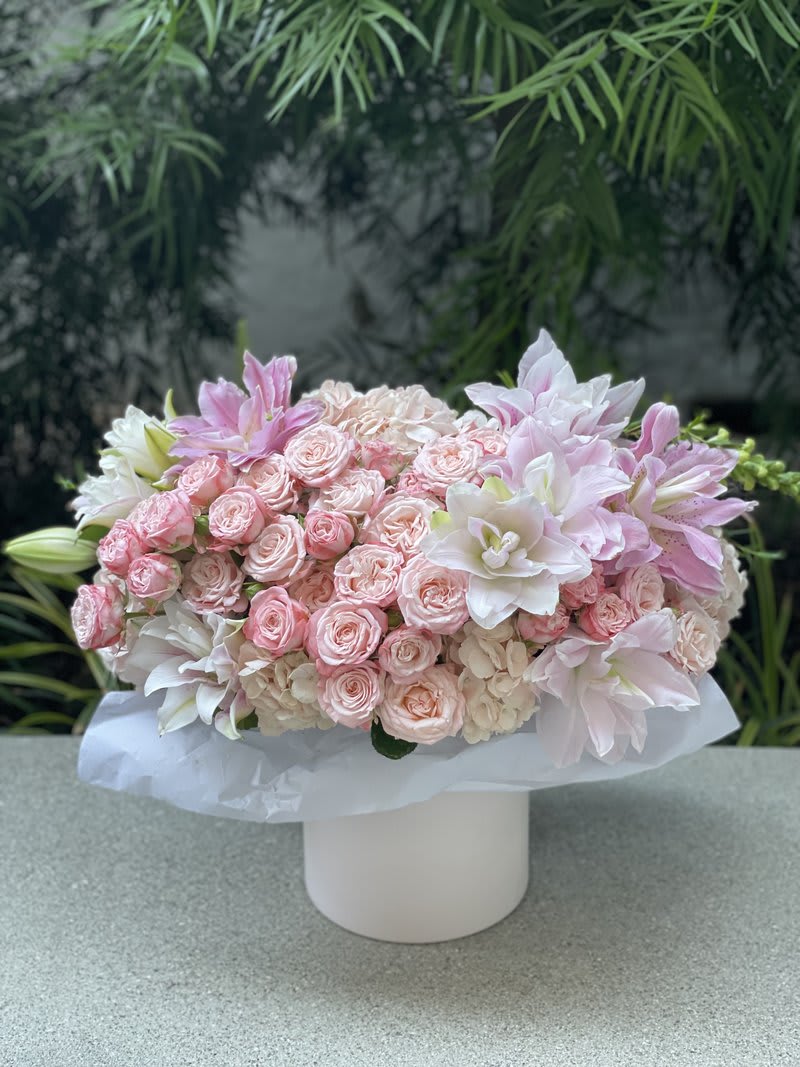 Pink roses and white lilies arranged in a white box vase