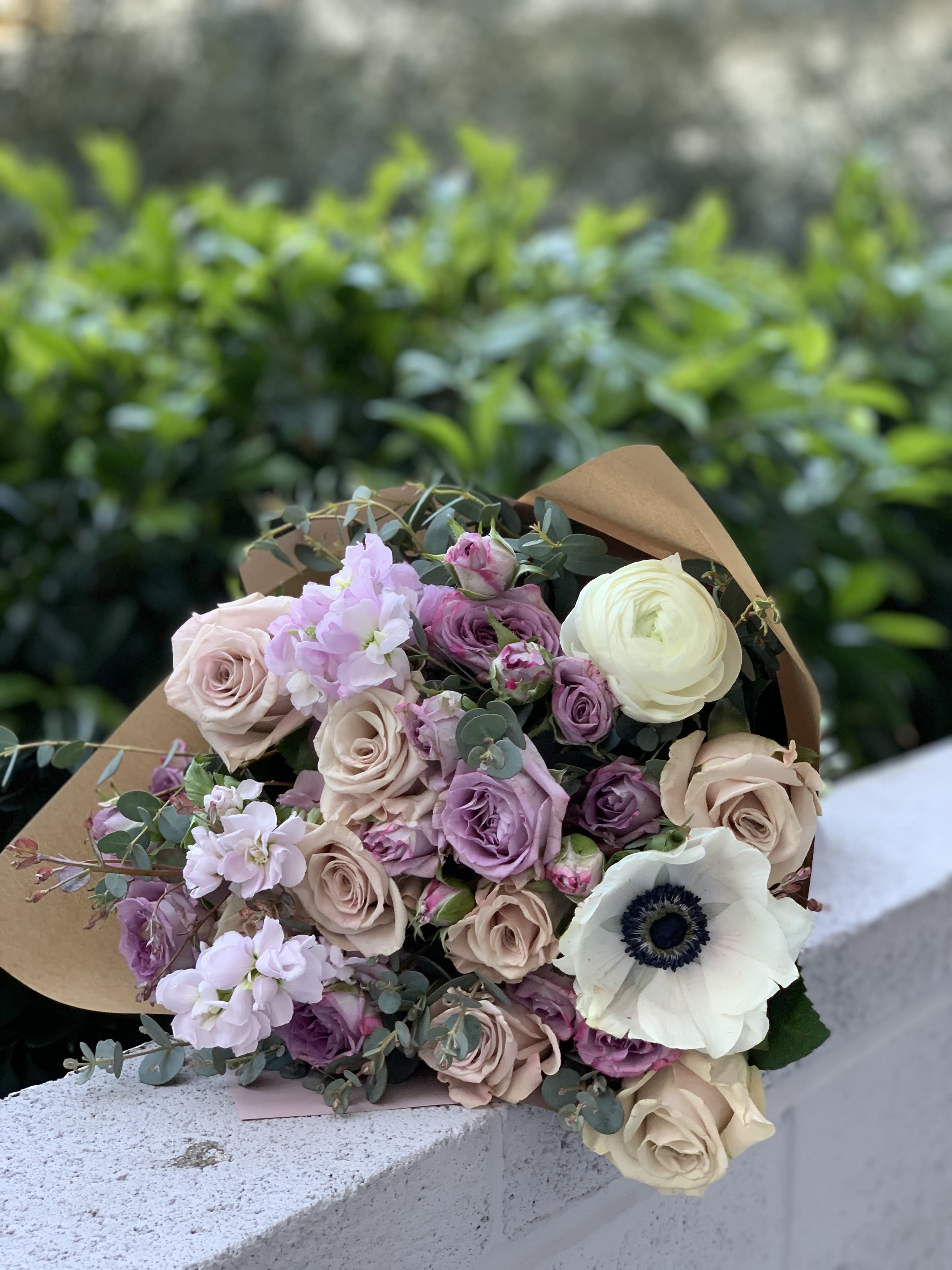 Bouquet of blush, lavender, and white flowers wrapped in brown paper