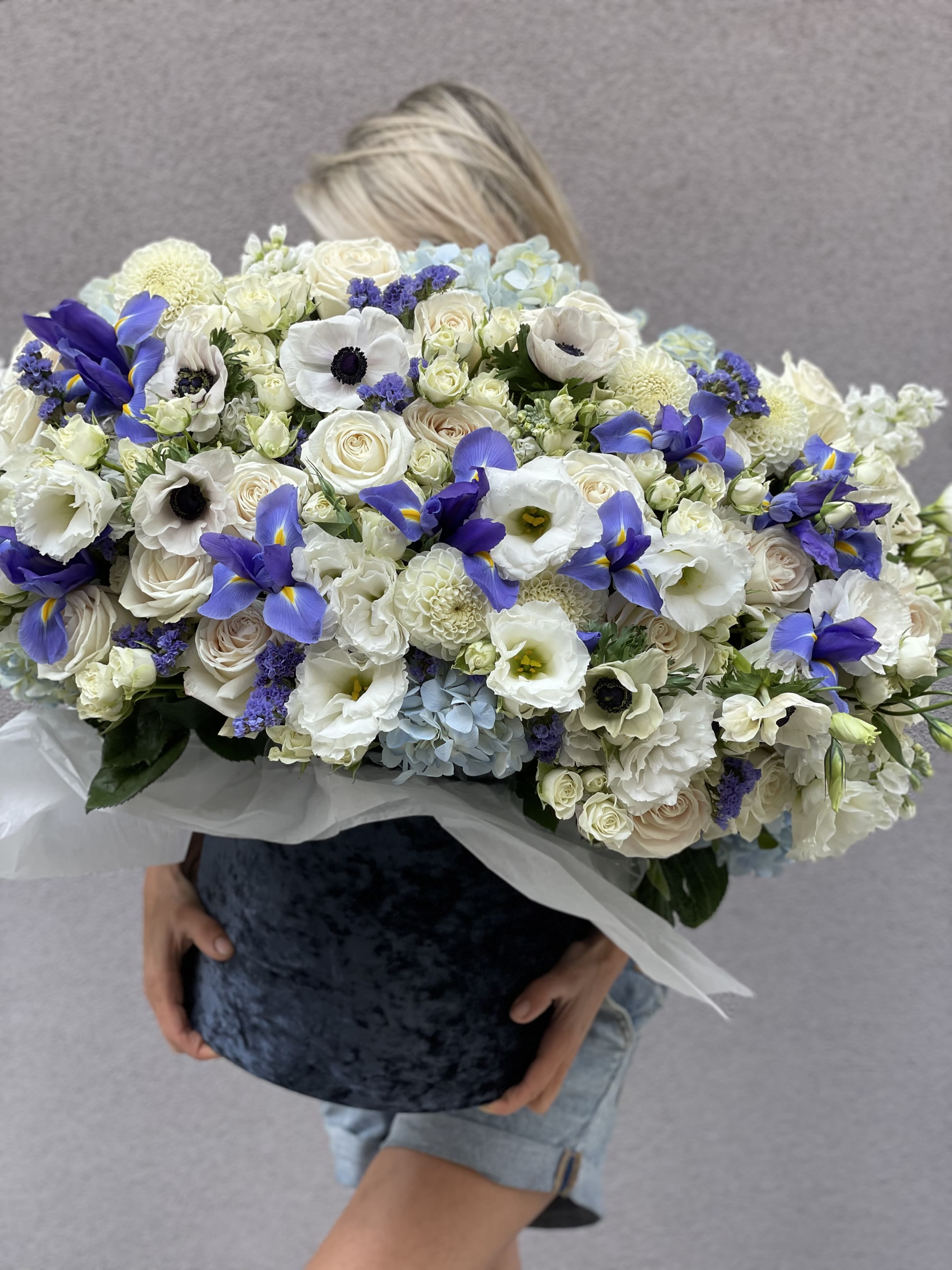 Large bouquet of white and blue flowers held in front of a person