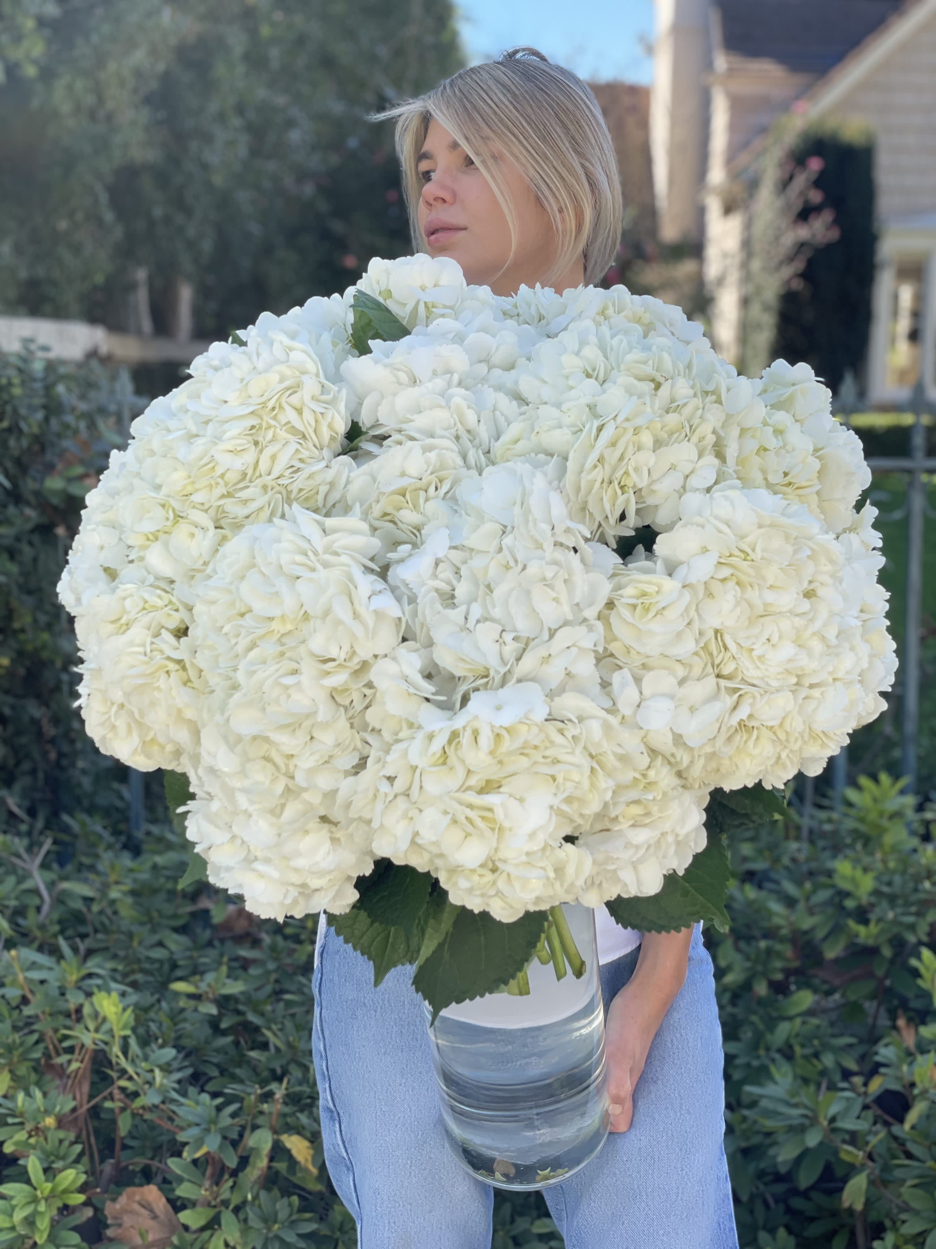Woman holding a large bouquet of white hydrangeas in a glass vase