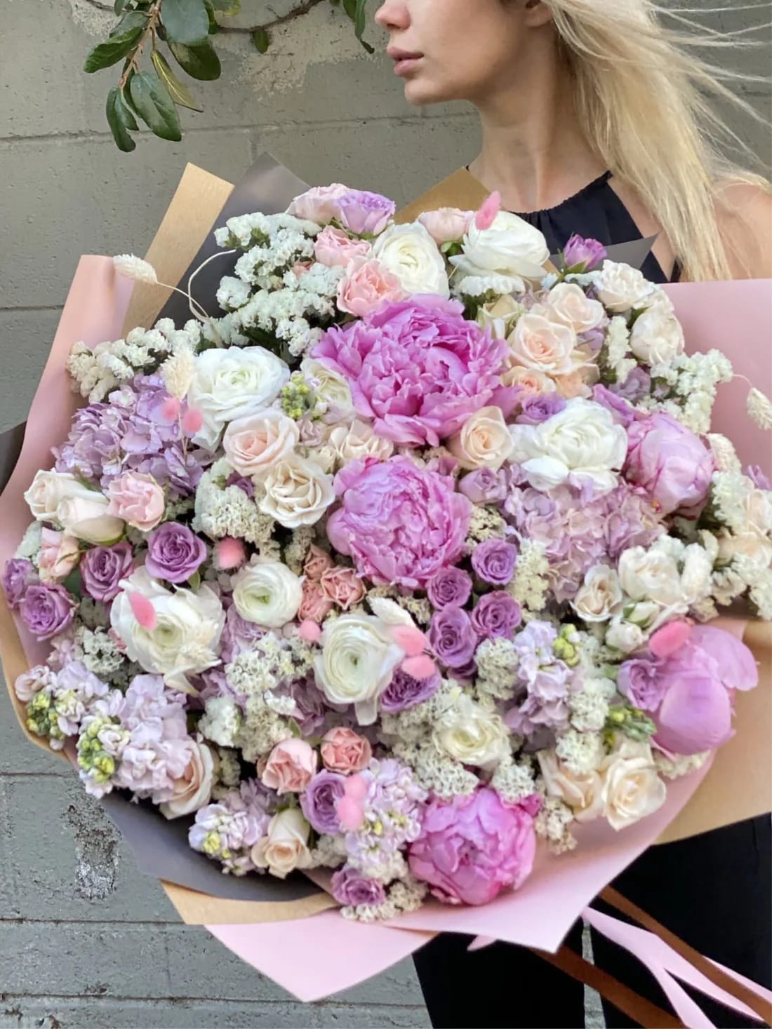 Large pastel bouquet of pink, lavender, and white flowers wrapped in paper
