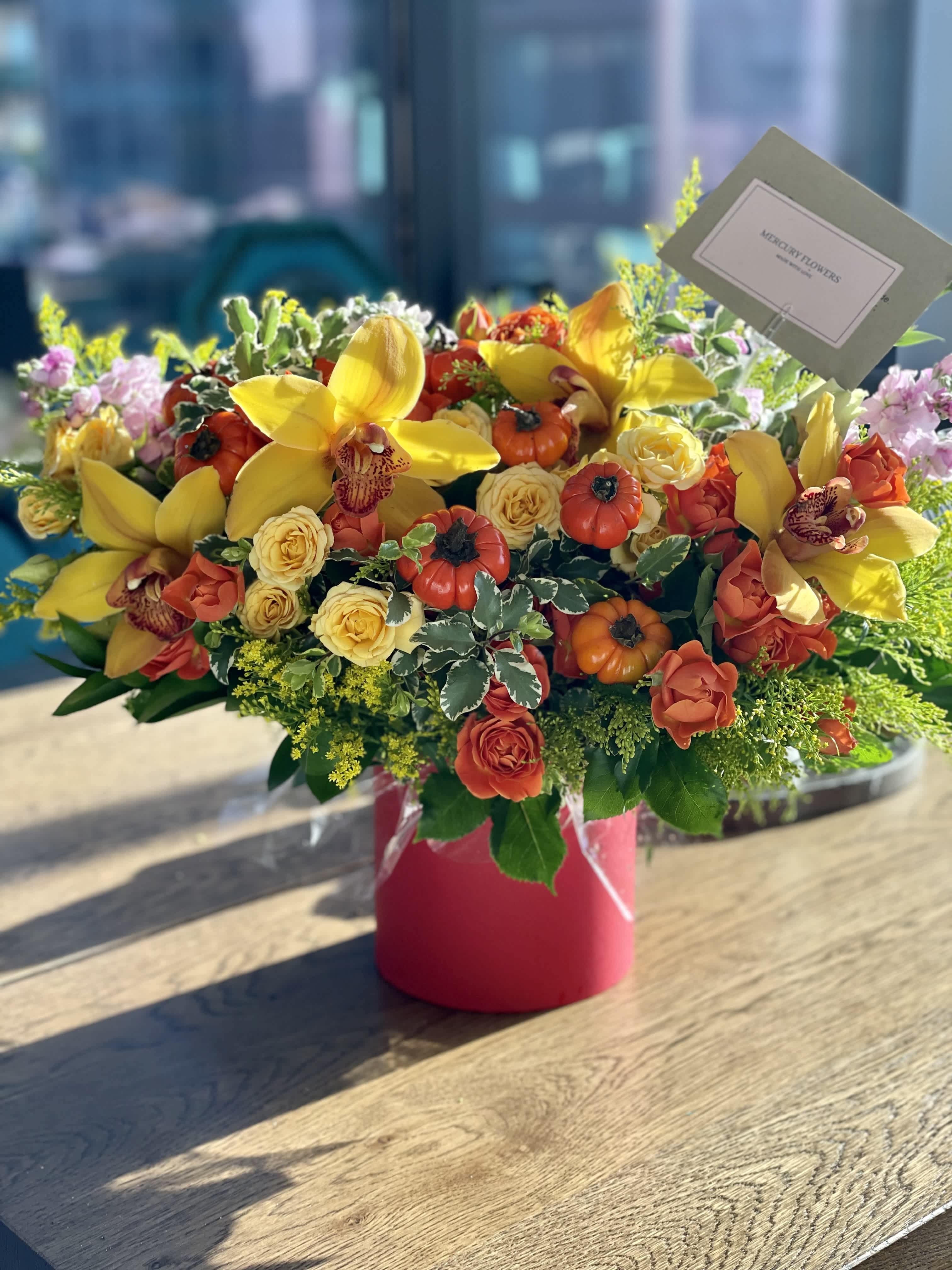 Bright mixed flower arrangement in a pink vase with yellow orchids and roses