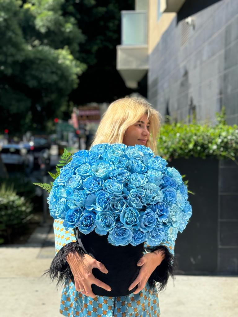 Woman holding a large bouquet of bright blue roses in a black vase