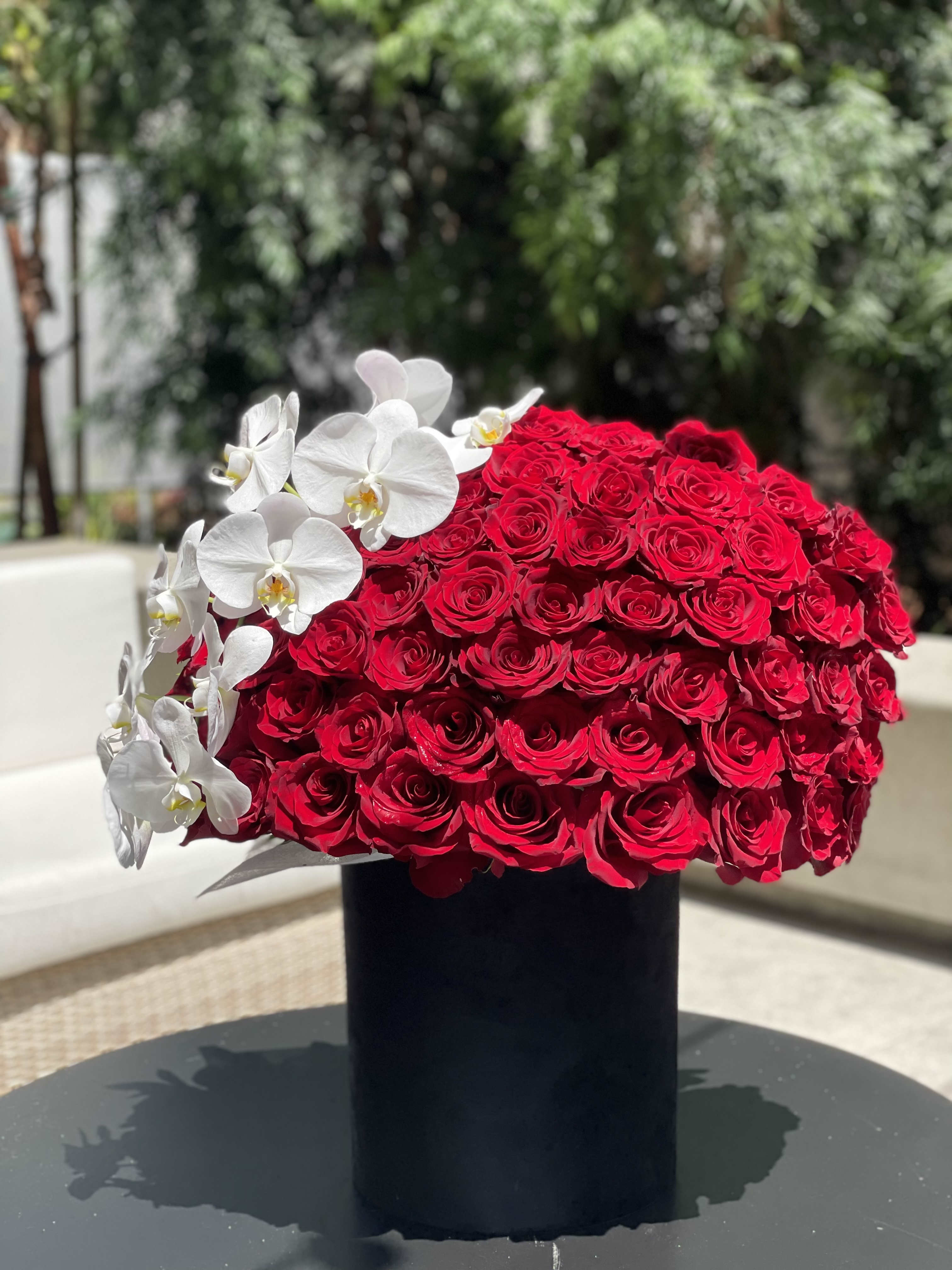 Large red rose arrangement with white orchids in a black vase