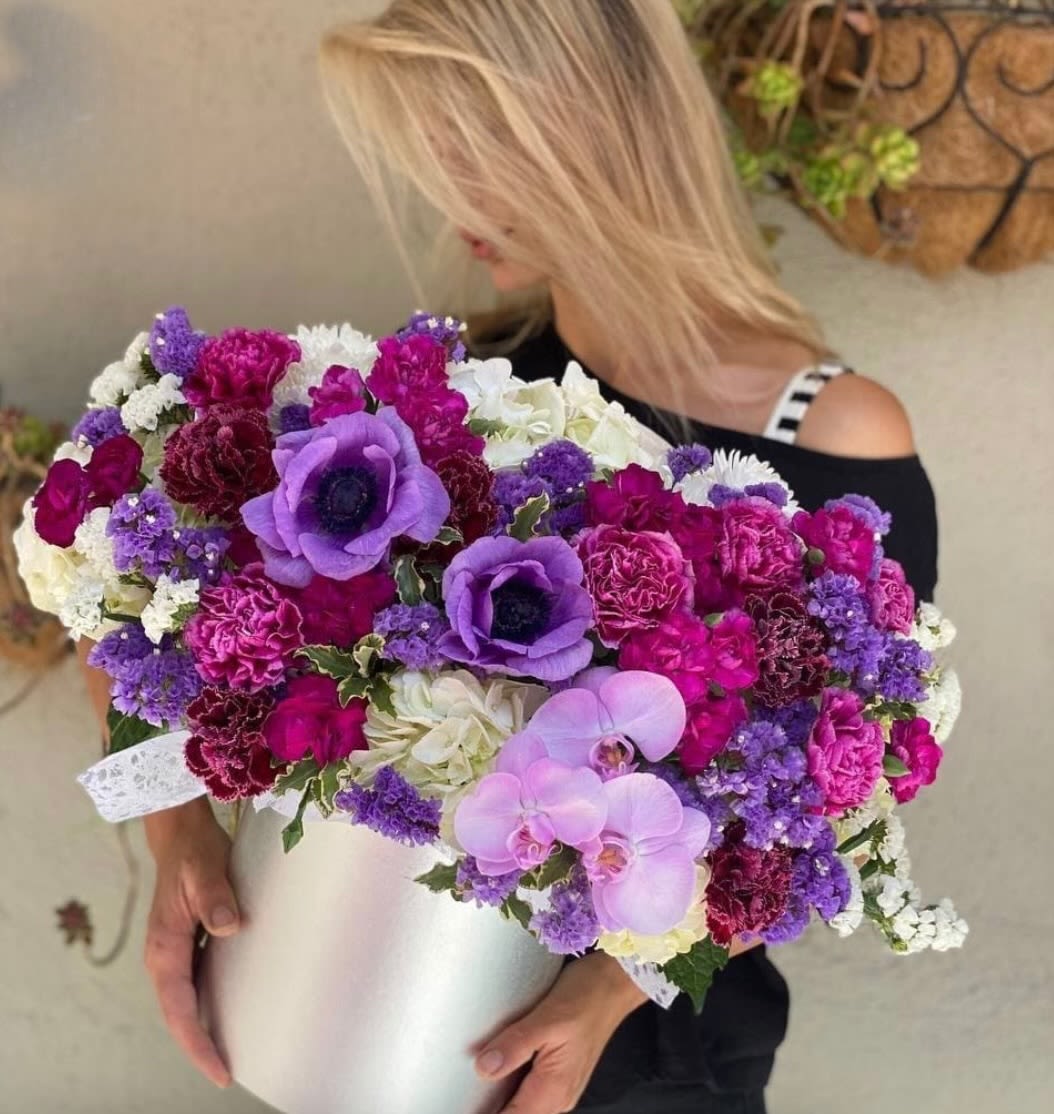 Woman holding a large purple, pink, and white flower arrangement in a white box
