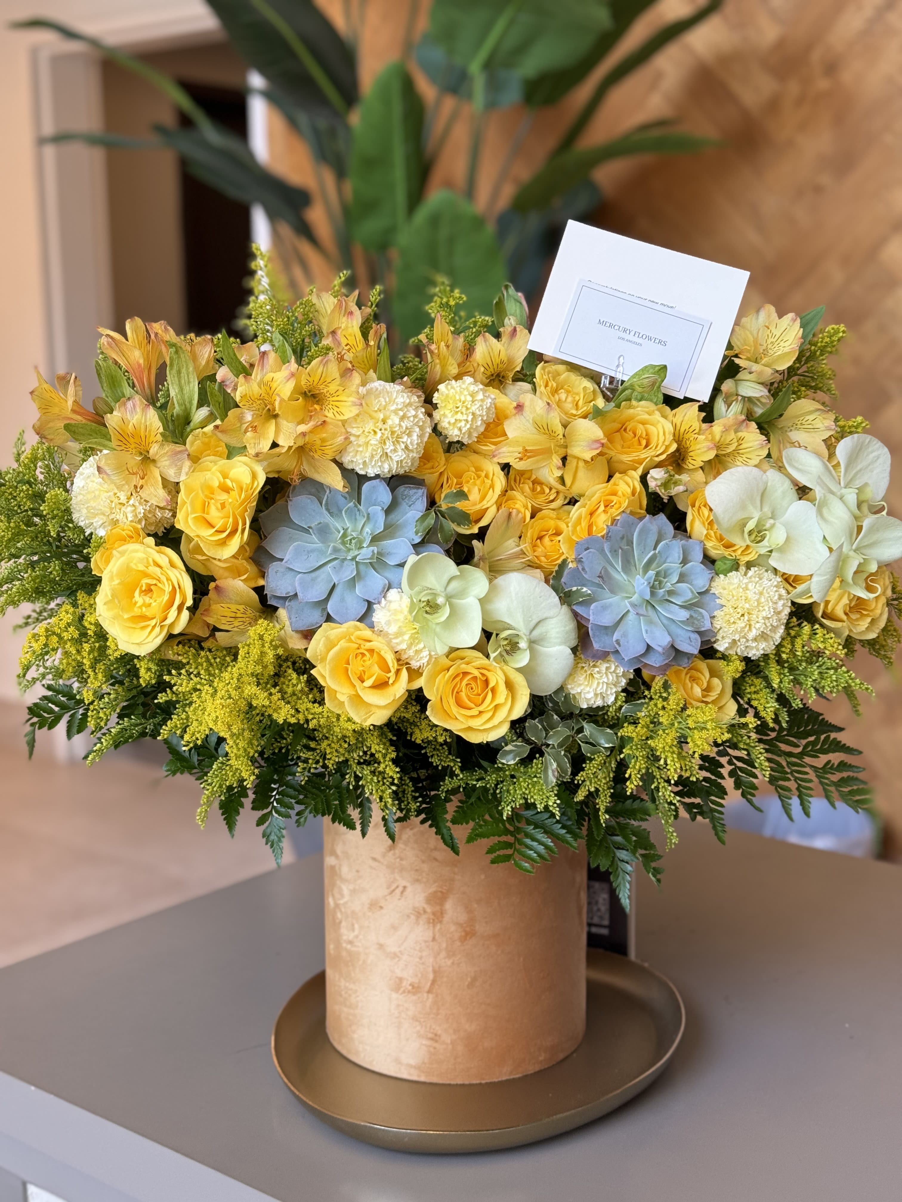 Yellow roses and orchids arranged in a gold hatbox