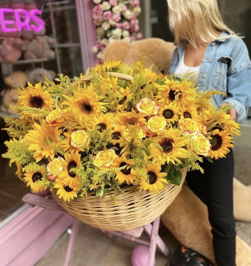 Large basket of yellow sunflowers and roses being held by a woman
