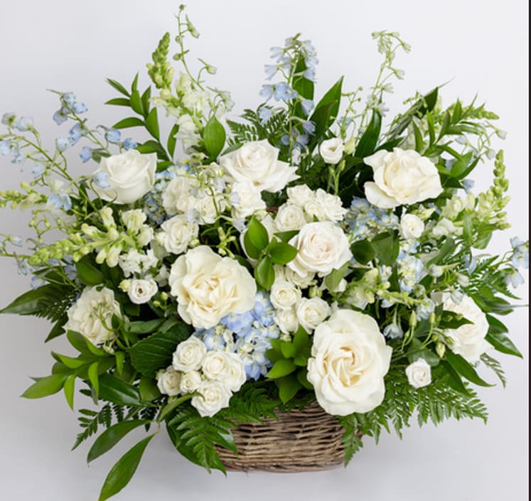 Large white and pale blue flower arrangement with roses in a wicker basket