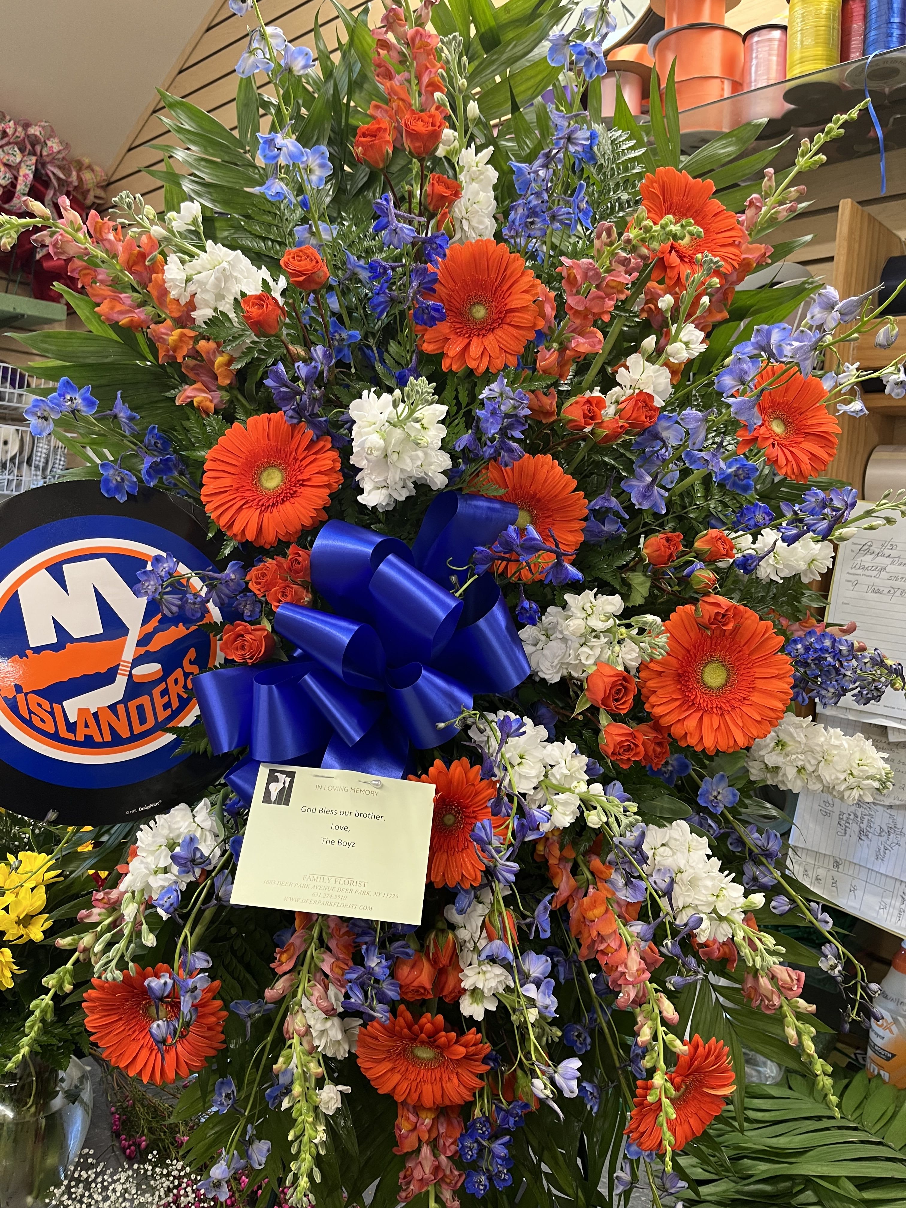 Large sympathy spray with orange gerberas, blue flowers, and white blooms