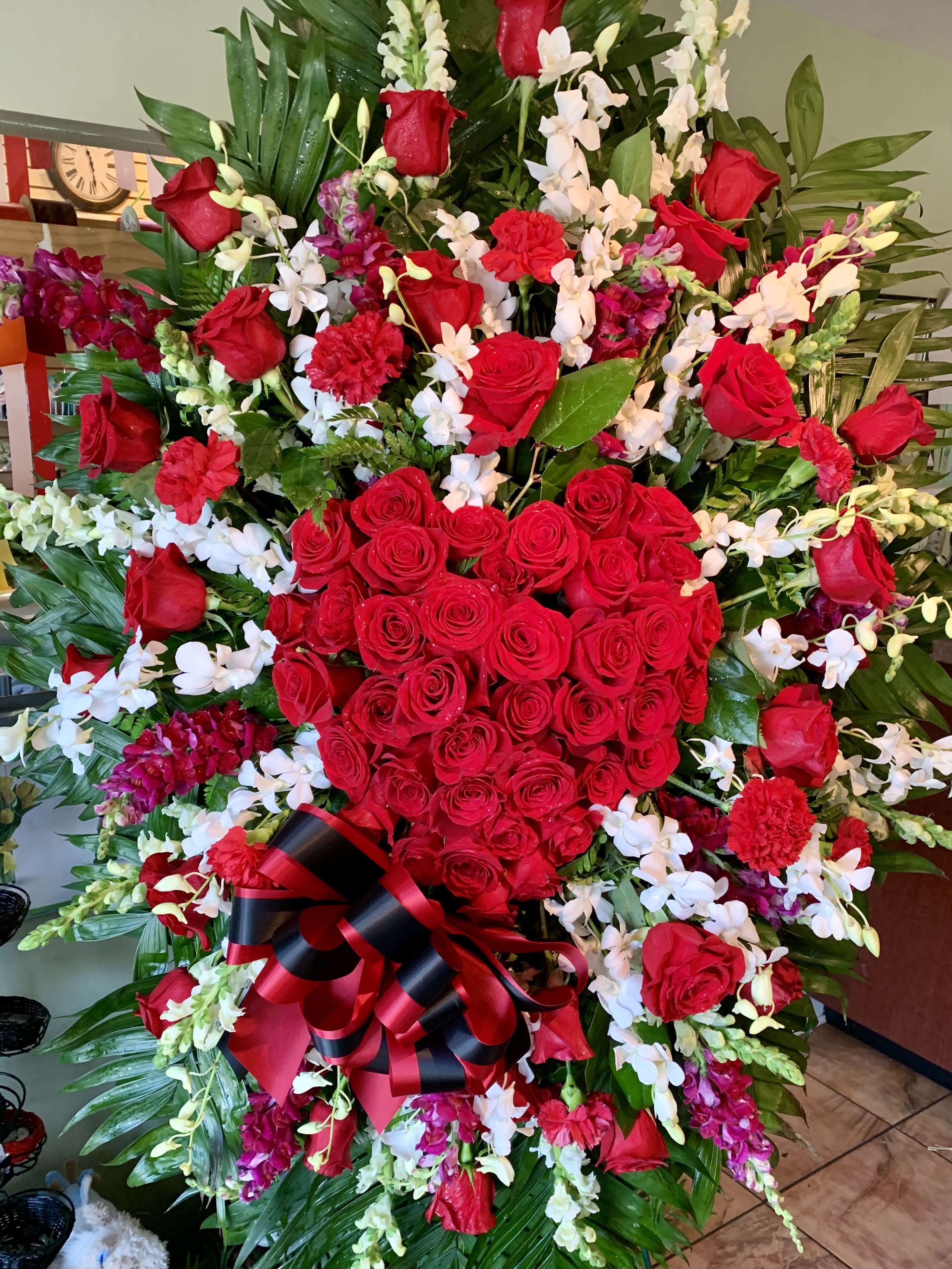 Large red rose and orchid standing spray with a black-and-red ribbon bow