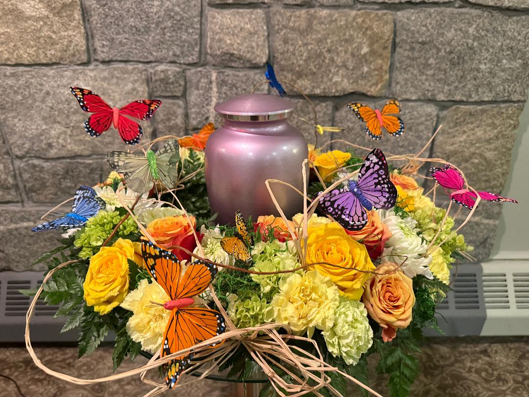 Butterfly-decorated floral arrangement around a pink urn