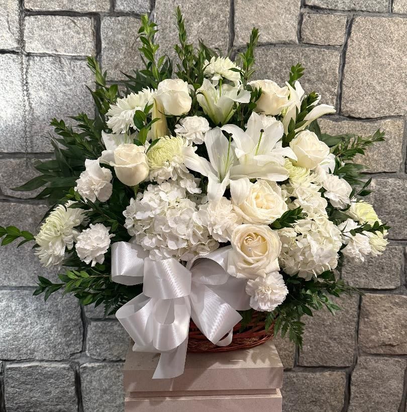 White floral arrangement with roses, lilies, and chrysanthemums in a basket with a ribbon