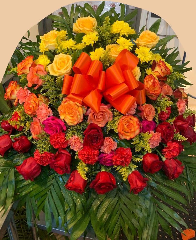 Large floral spray of red, orange, and yellow roses with a bright ribbon bow