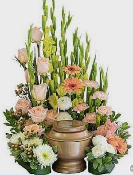 Tall floral arrangement with peach roses, gerbera daisies, and white blooms in a bronze urn