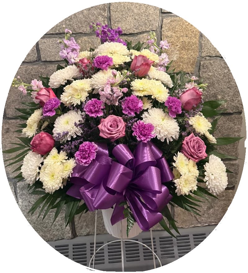 Pink and white floral spray with a purple ribbon bow in a white stand