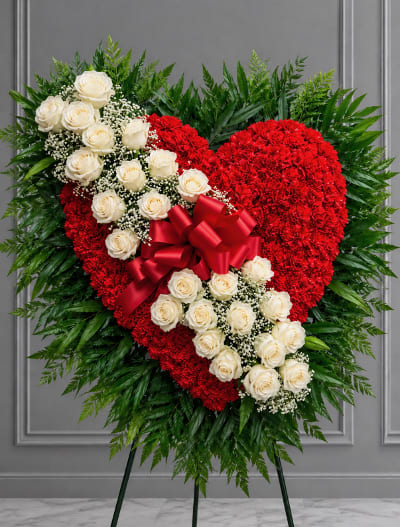 Heart-shaped red floral tribute with white roses and a red bow on an easel