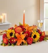 Low floral centerpiece with orange lilies, sunflowers, and red roses around a candle