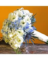 Hand-tied white and blue bridal bouquet with roses, calla lilies, hydrangea and thistle on a rustic surface