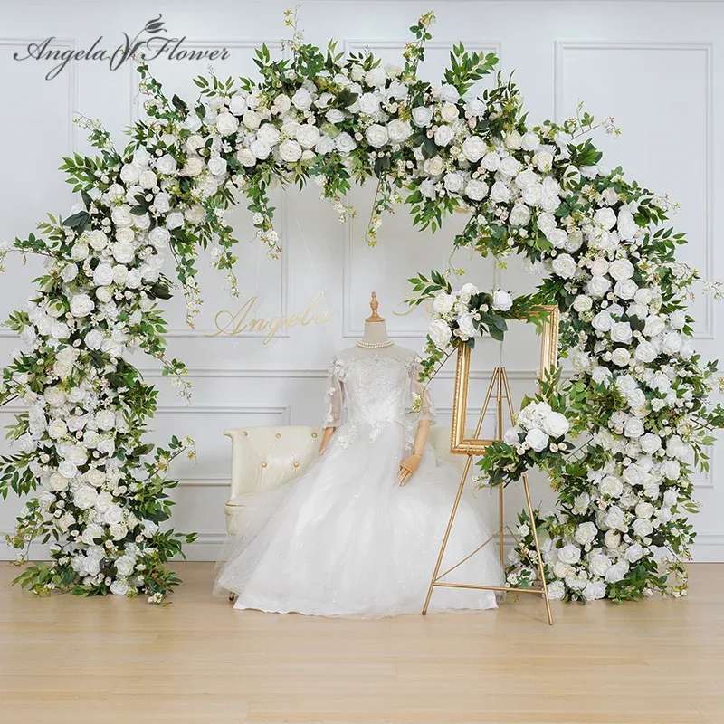 Large white rose wedding arch with matching floral frame beside a mannequin in a bridal gown and chair.