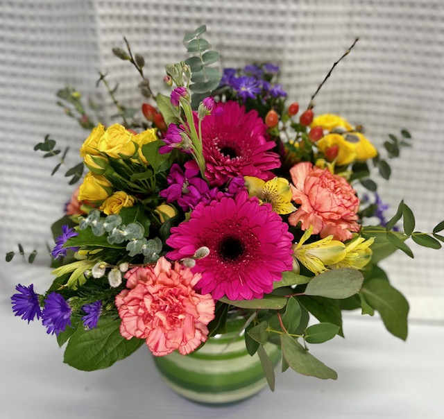 Bright mixed bouquet in a green-striped vase with pink, yellow, and purple flowers