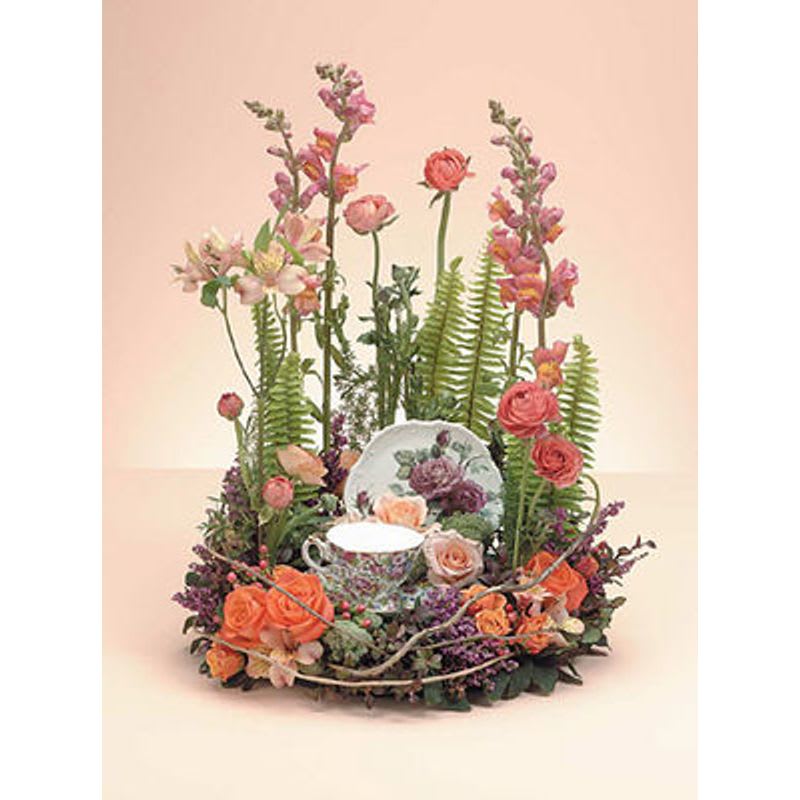 Floral arrangement with roses and snapdragons around a teacup and saucer