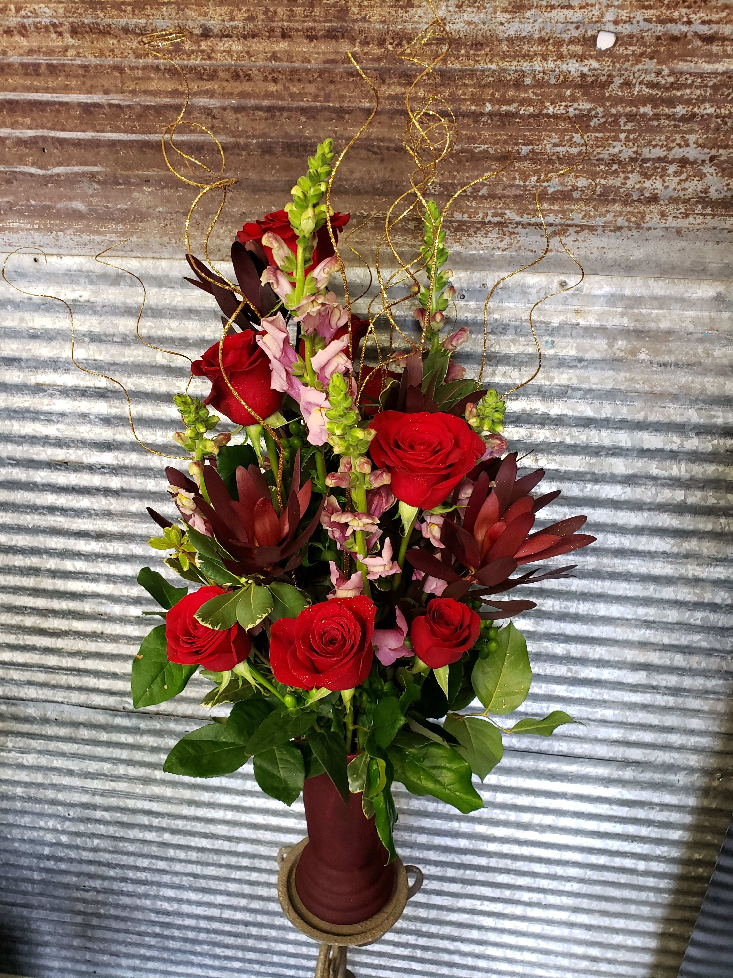 Tall arrangement of red roses and pink snapdragons in a burgundy vase