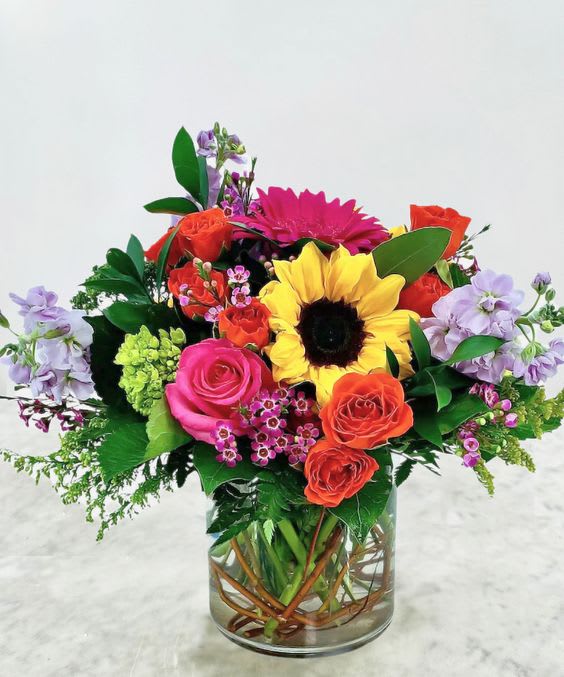 Colorful mixed bouquet in a clear glass vase with a sunflower and roses
