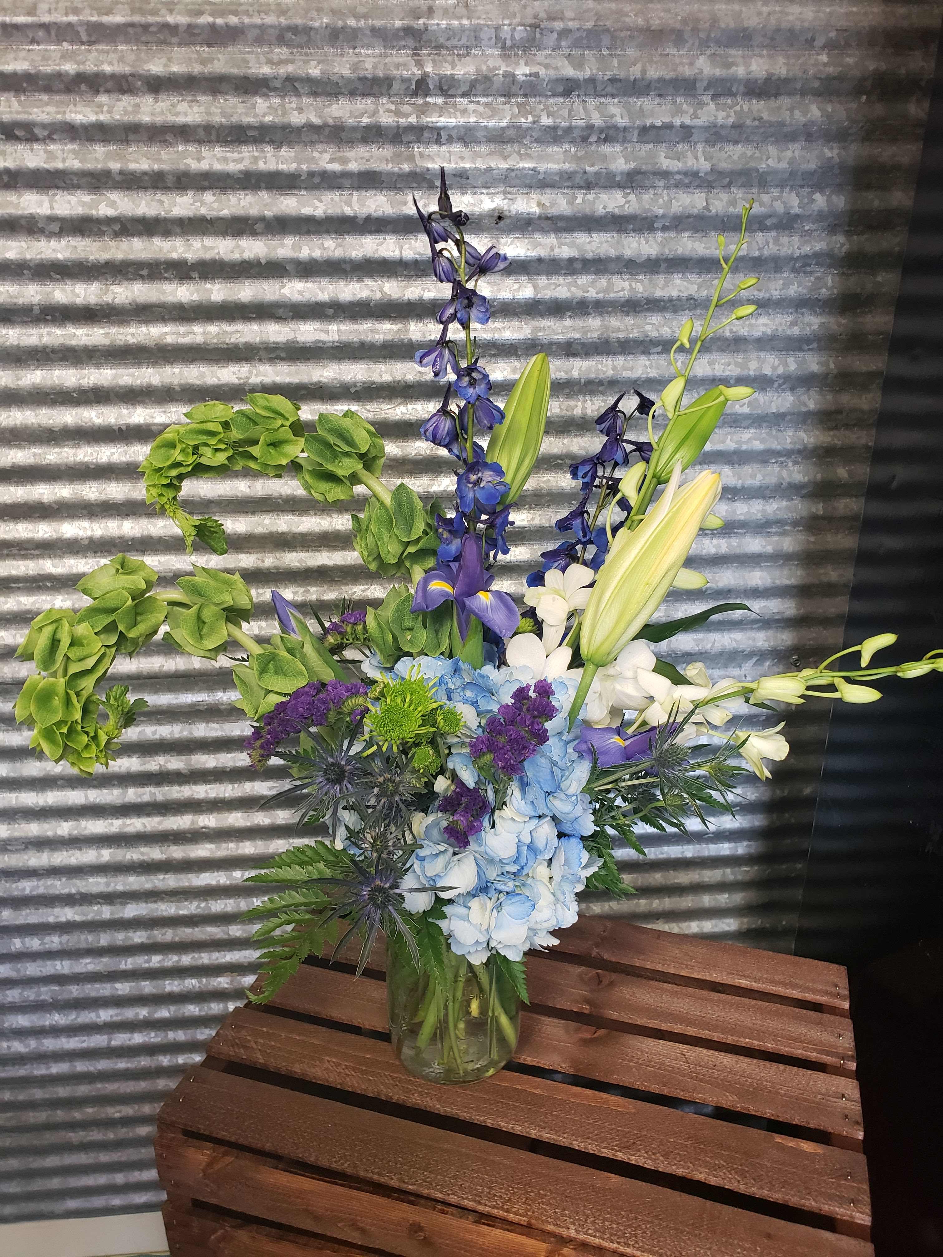 Blue and Green vase - An eye-catching mix of Blue, Green, and white flowers in a vase. Orchids, Lilies, Iris, Bells and Delphinium and Sea thistle  