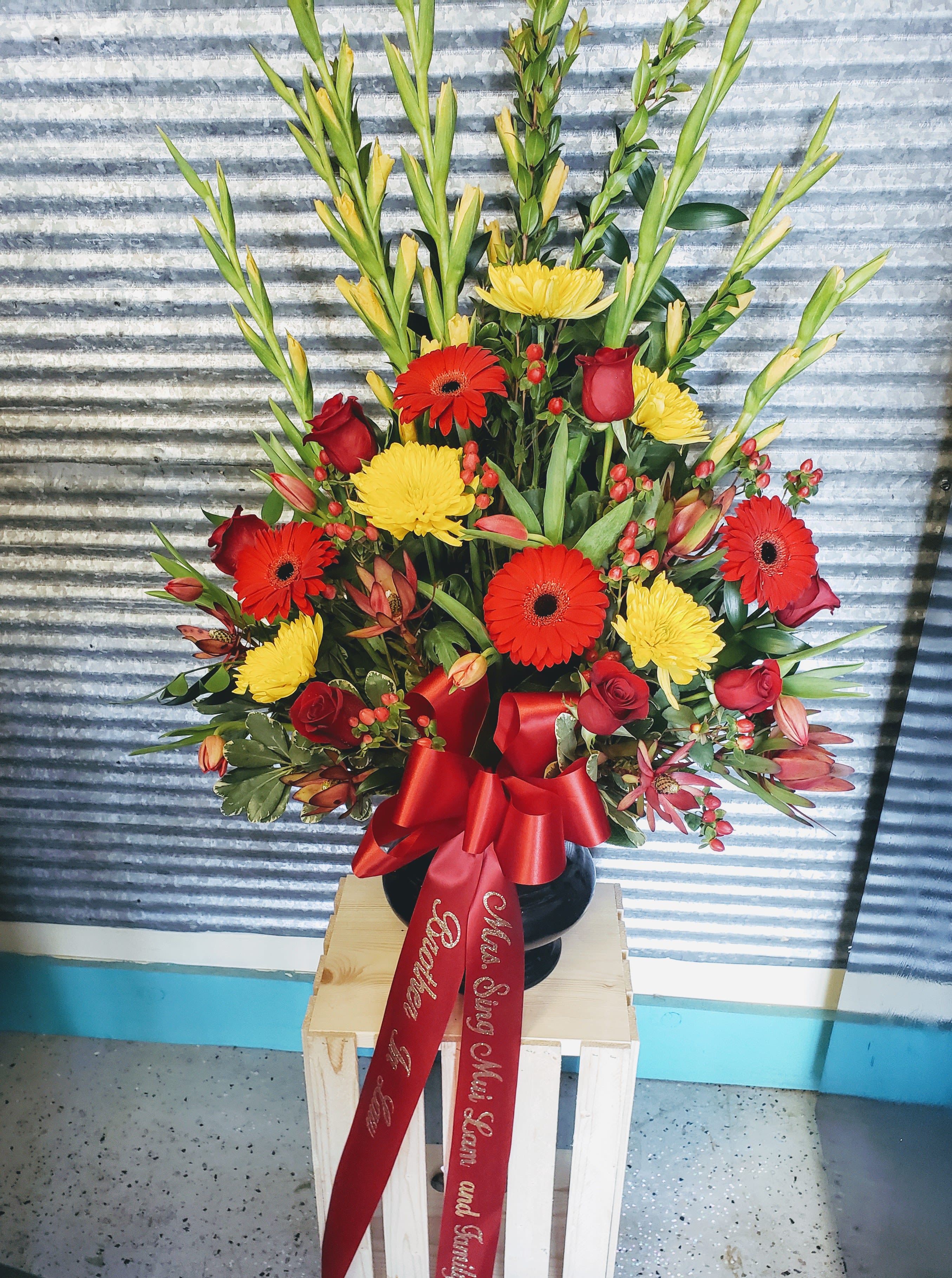 Tall floral arrangement with red roses, gerbera daisies, and yellow blooms in a black vase