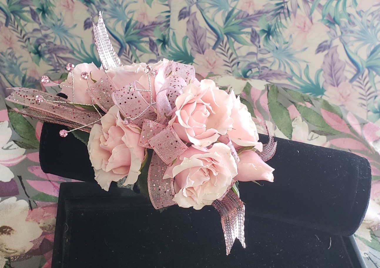 Pink rose corsage with glittery ribbon on a black display stand