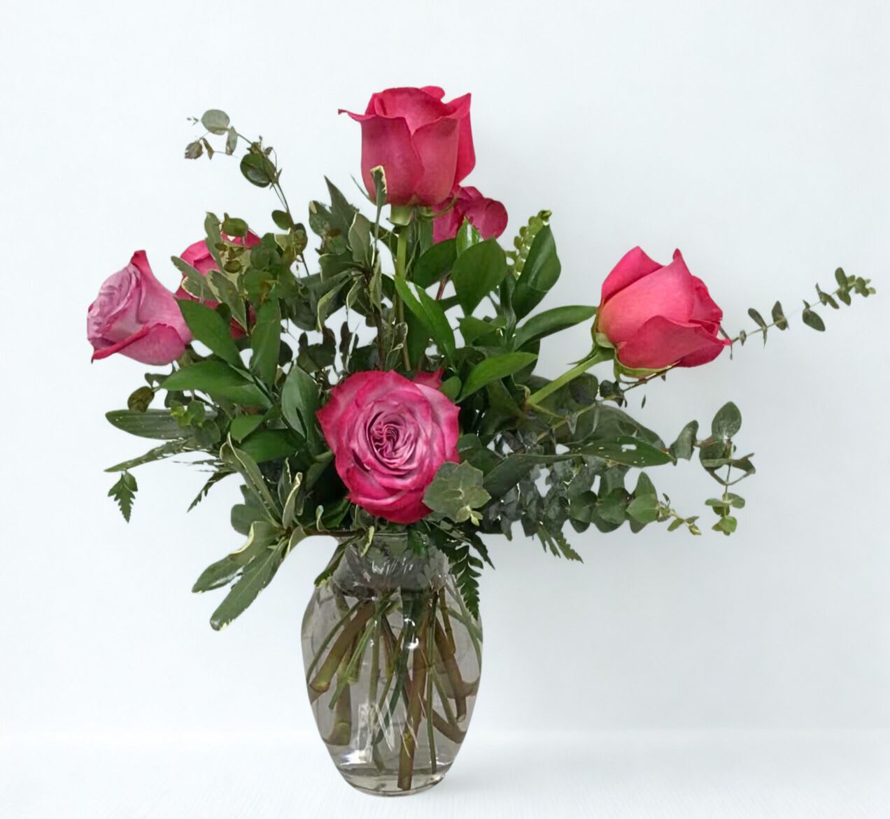 Pink roses arranged in a clear glass vase with greenery