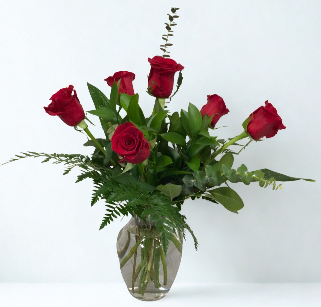 Red roses arranged in a clear glass vase with greenery
