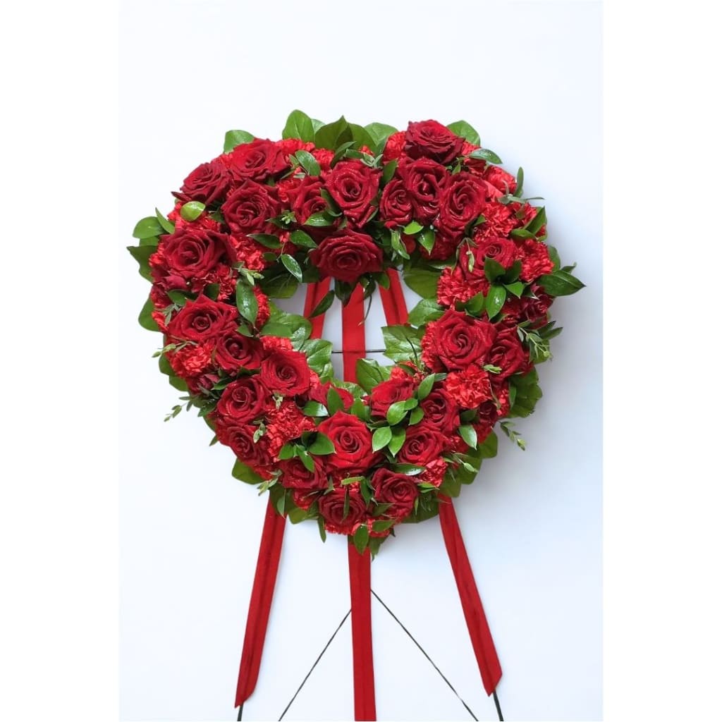 Heart-shaped red rose wreath on a stand with ribbon tails