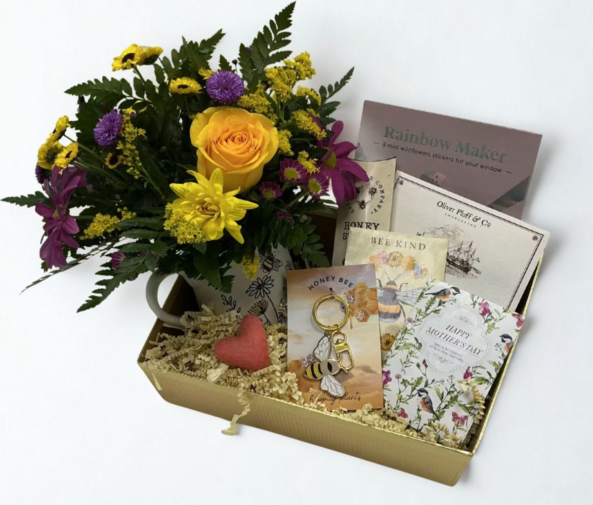 Queen Bee Bloom Box - Celebrate Mom like the queen she is with our Queen Bee Bloom Box — a beautifully curated Mother’s Day gift full of sweetness, charm, and a touch of nature.  A beautiful keepsake mug filled with a fresh floral arrangement, bringing instant beauty to her day!  She’ll enjoy a cozy moment with tea from Oliver Pluff &amp; Co. paired with golden honey sticks and for a little extra sparkle, we’ve included a Queen Bee purse charm by Happily Plants, a lovely reminder of her strength and grace. A beautiful seed packet card personalized with your message invites her to plant something beautiful and watch it grow.  Sweet, uplifting, and fit for a queen, this Bloom Box is the perfect way to show Mom how much she means.