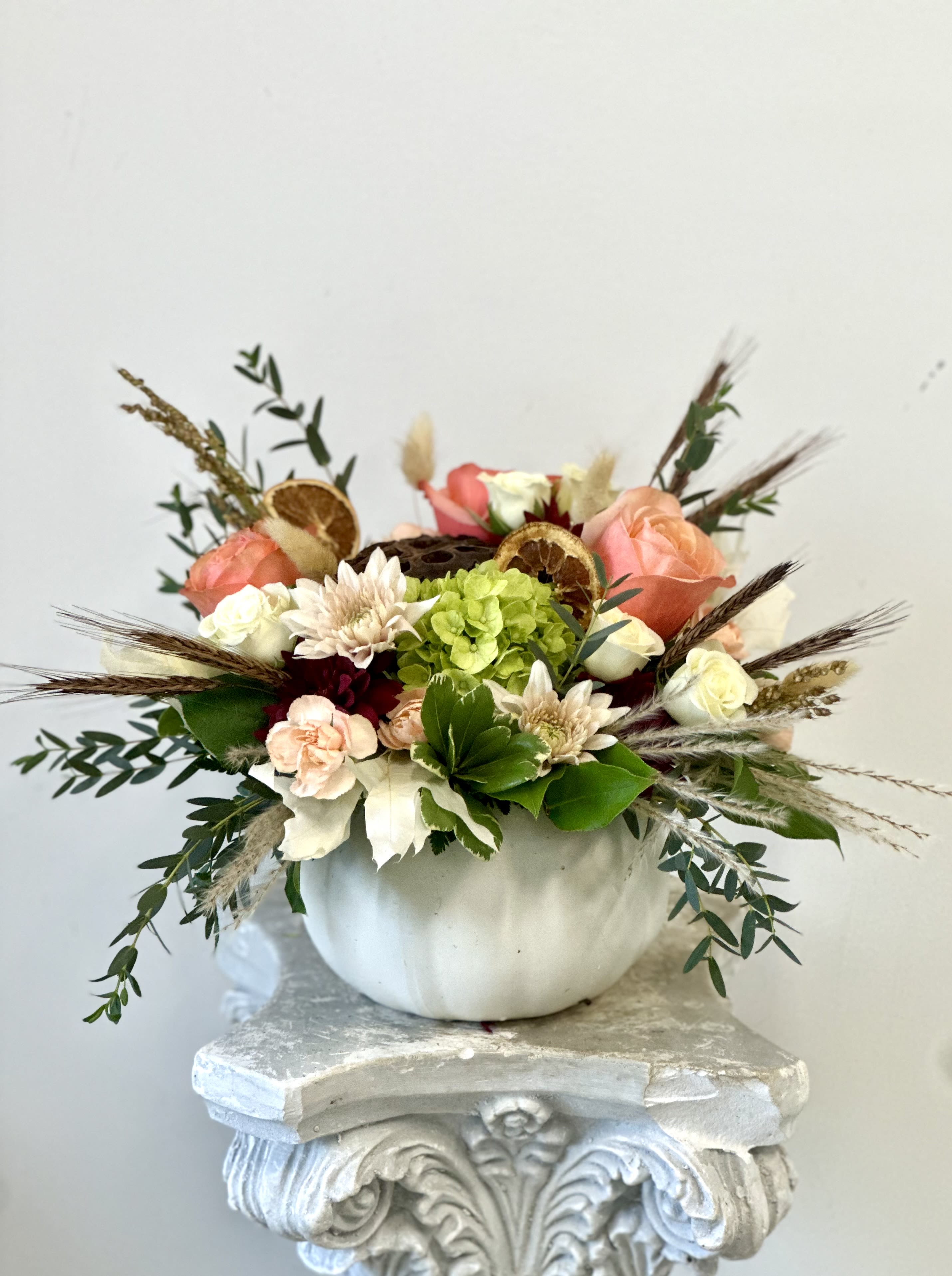 Fall Fusion by Westford Florist Art by Veny - Elevate your autumn décor with Fall Fusion by Westford Florist Art by Veny, a stunning arrangement that captures the essence of the season. This exquisite selection features elegant peach roses and delicate spray roses paired harmoniously with peach poms and mini green hydrangea. Accented by peach mini carnations, carnations, dry orange slices, whimsical pampas grass, this ensemble is artfully displayed in a chic white pumpkin. Perfect for home decoration, Halloween or as an eye-catching centerpiece for gatherings, Fall Fusion brings warmth and sophistication to any space. Embrace the beauty of fall while creating an inviting atmosphere for friends and family alike. Transform your surroundings effortlessly with this unique floral masterpiece—your perfect seasonal statement awaits!