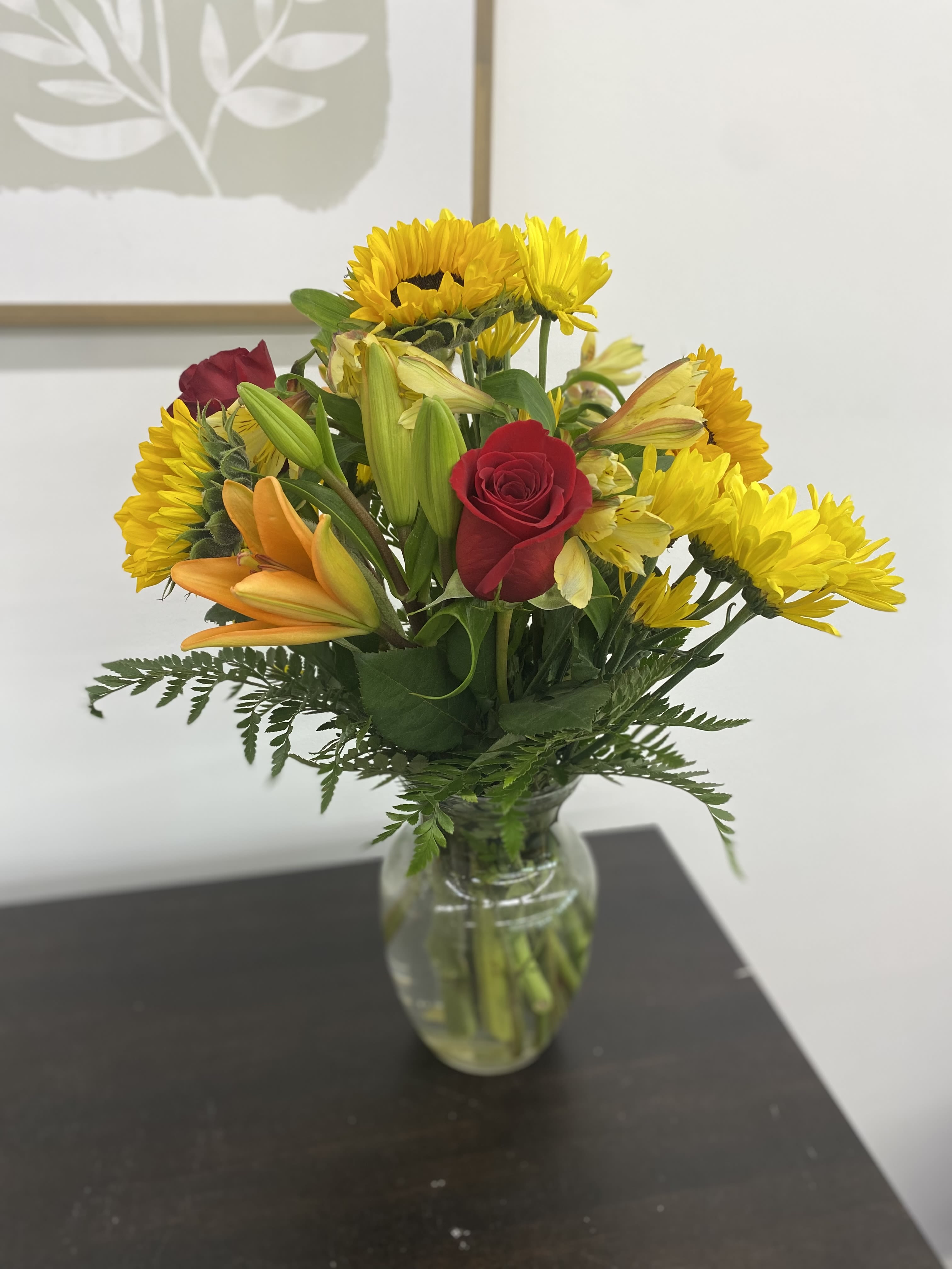 Mixed bouquet of yellow daisies, red roses, and orange lilies in a glass vase