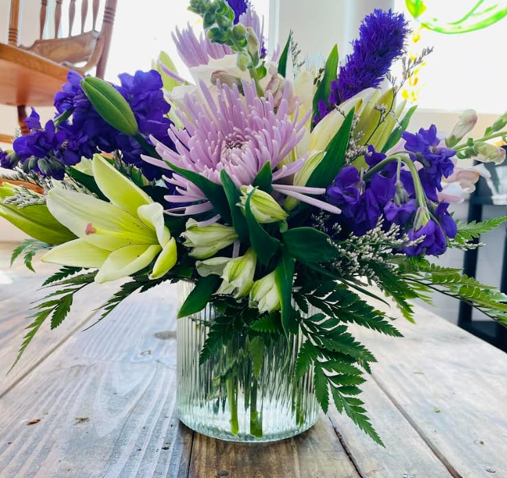 Purple and white mixed flower arrangement in a clear glass vase