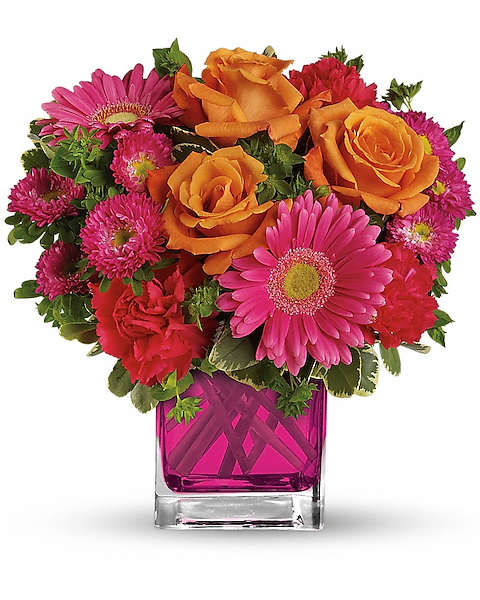 Pink gerberas, orange roses, and magenta flowers in a square glass vase