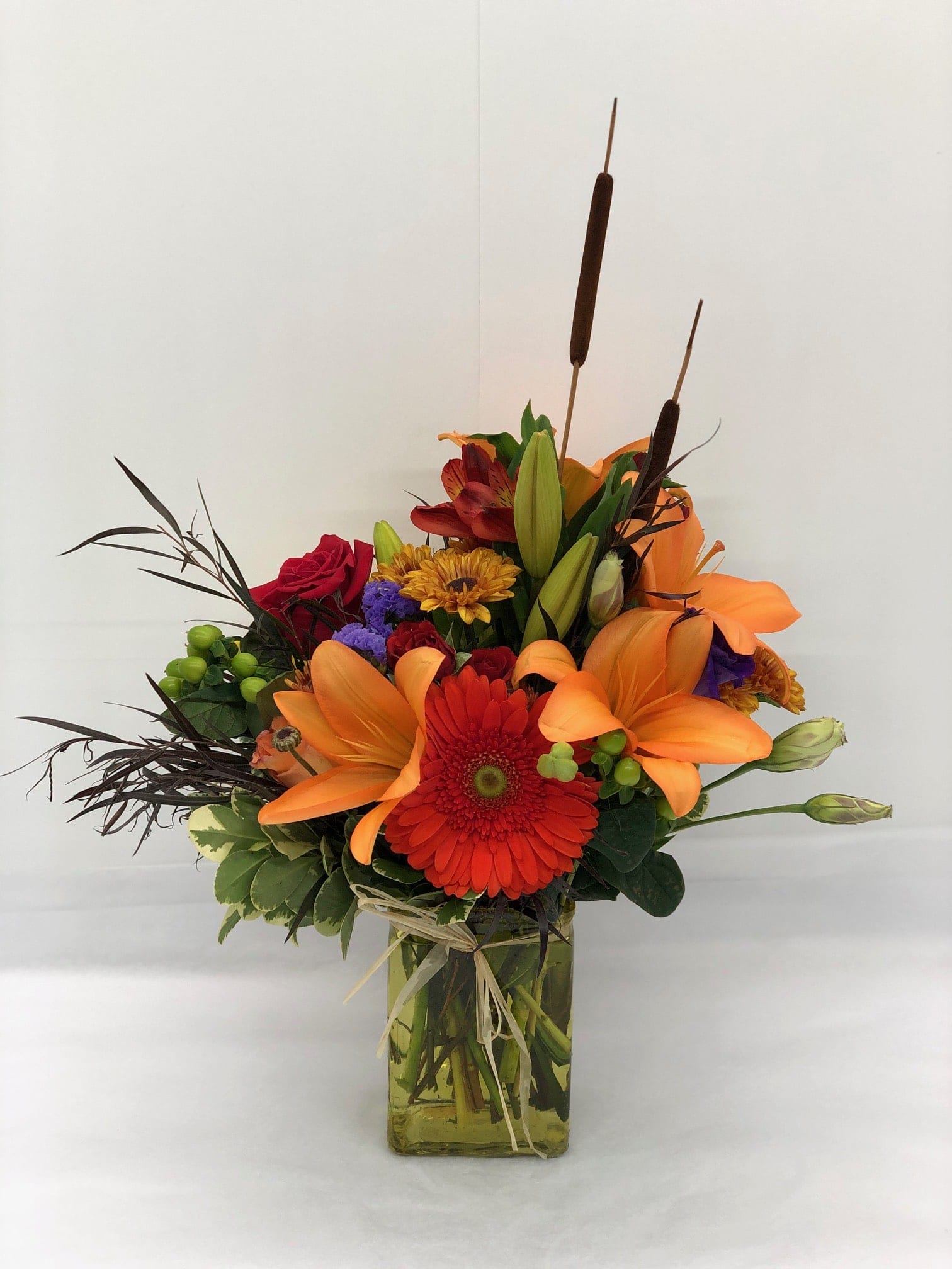 Leaves by the River Bouquet - Bright and bold fall colors accented with some fall greenery and dried cattails that are sure to brighten up those cloudy days. (Standard arranged in a short rectangular green vase, premium will be in a tall rectangular vase and COLORS MAY VARY.)  Flowers and colors may be substituted depending on availability. 