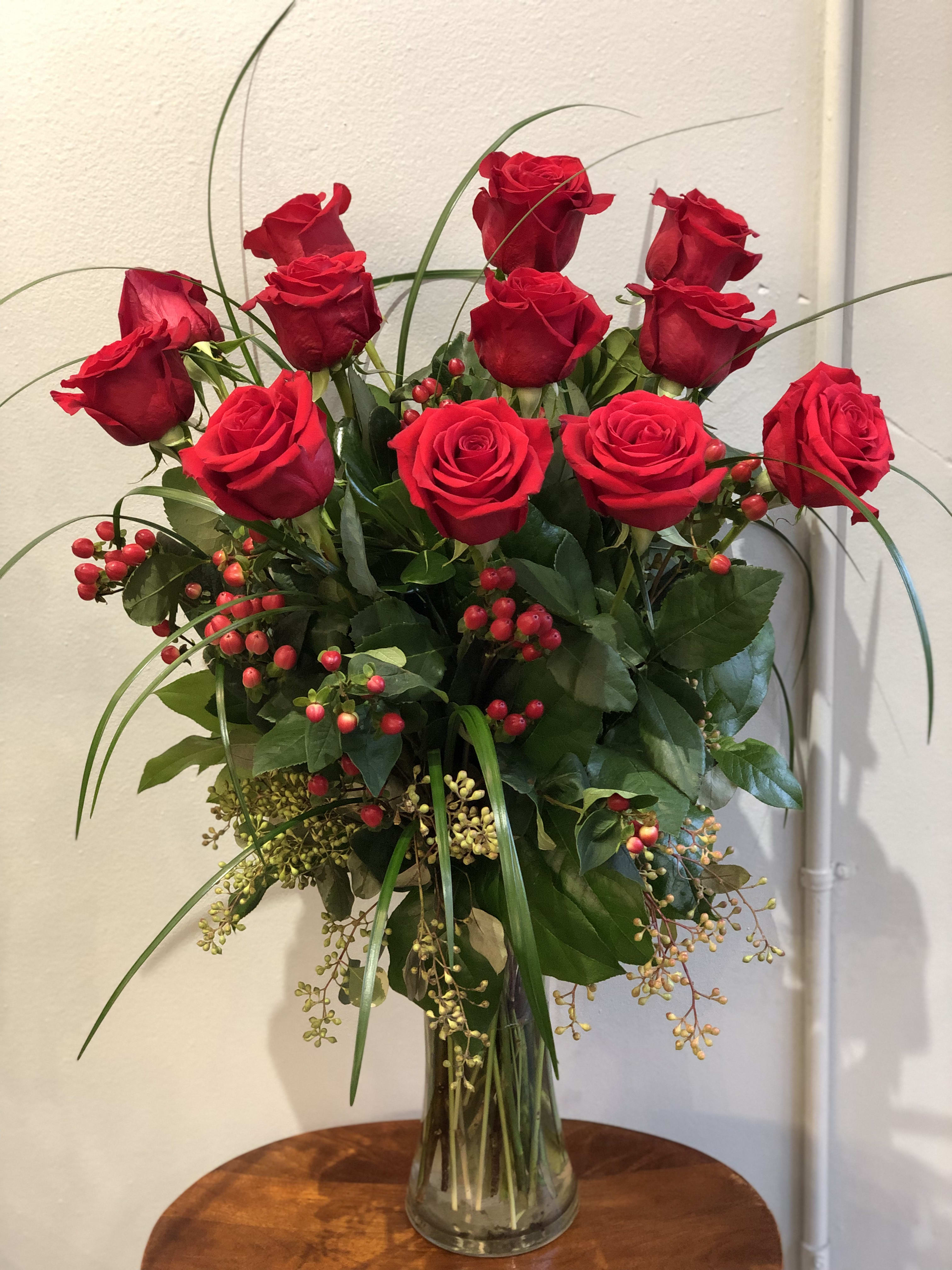 Red roses arranged in a clear glass vase with berries and greenery