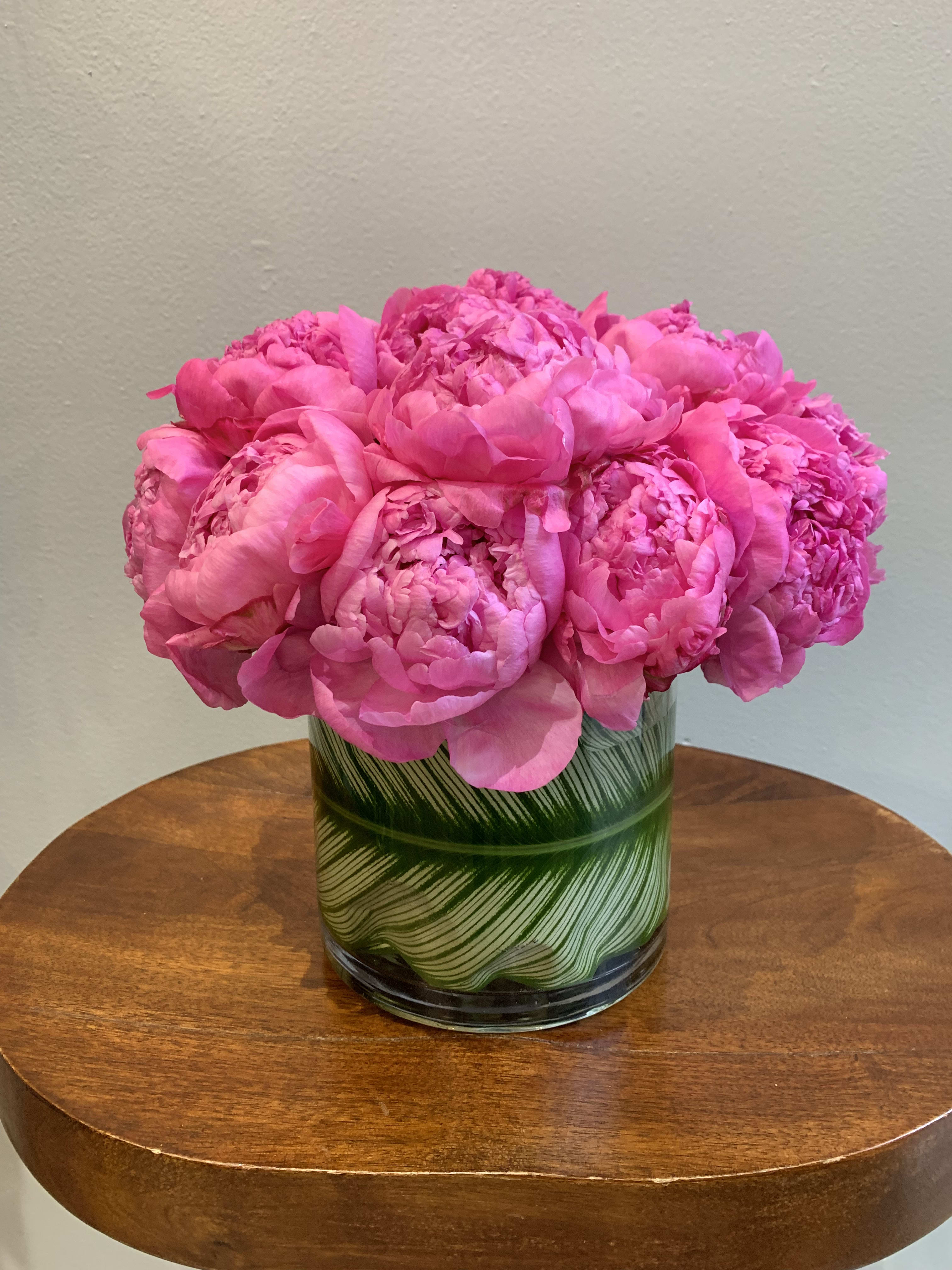 Pink peonies arranged in a glass vase with green leaf pattern