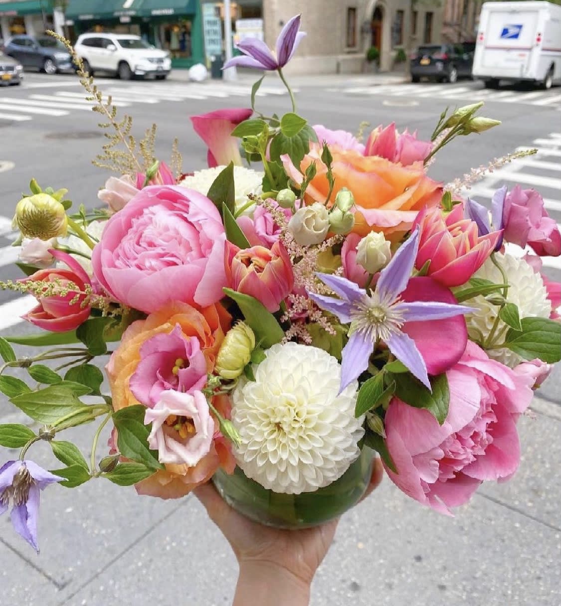 Handheld bouquet of pink, peach, and purple flowers in a glass vase