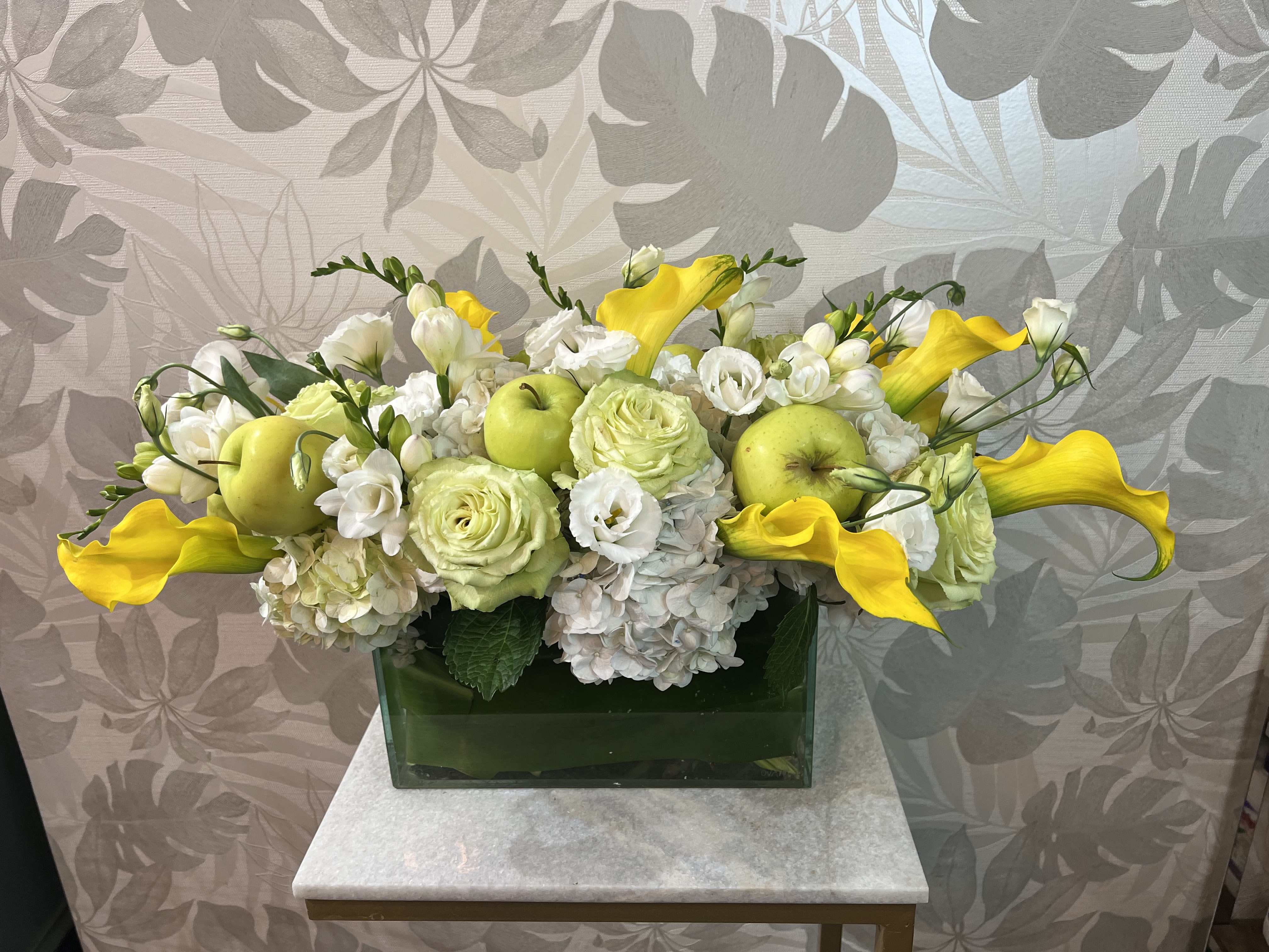 Yellow calla lilies and white flowers arranged in a green rectangular vase