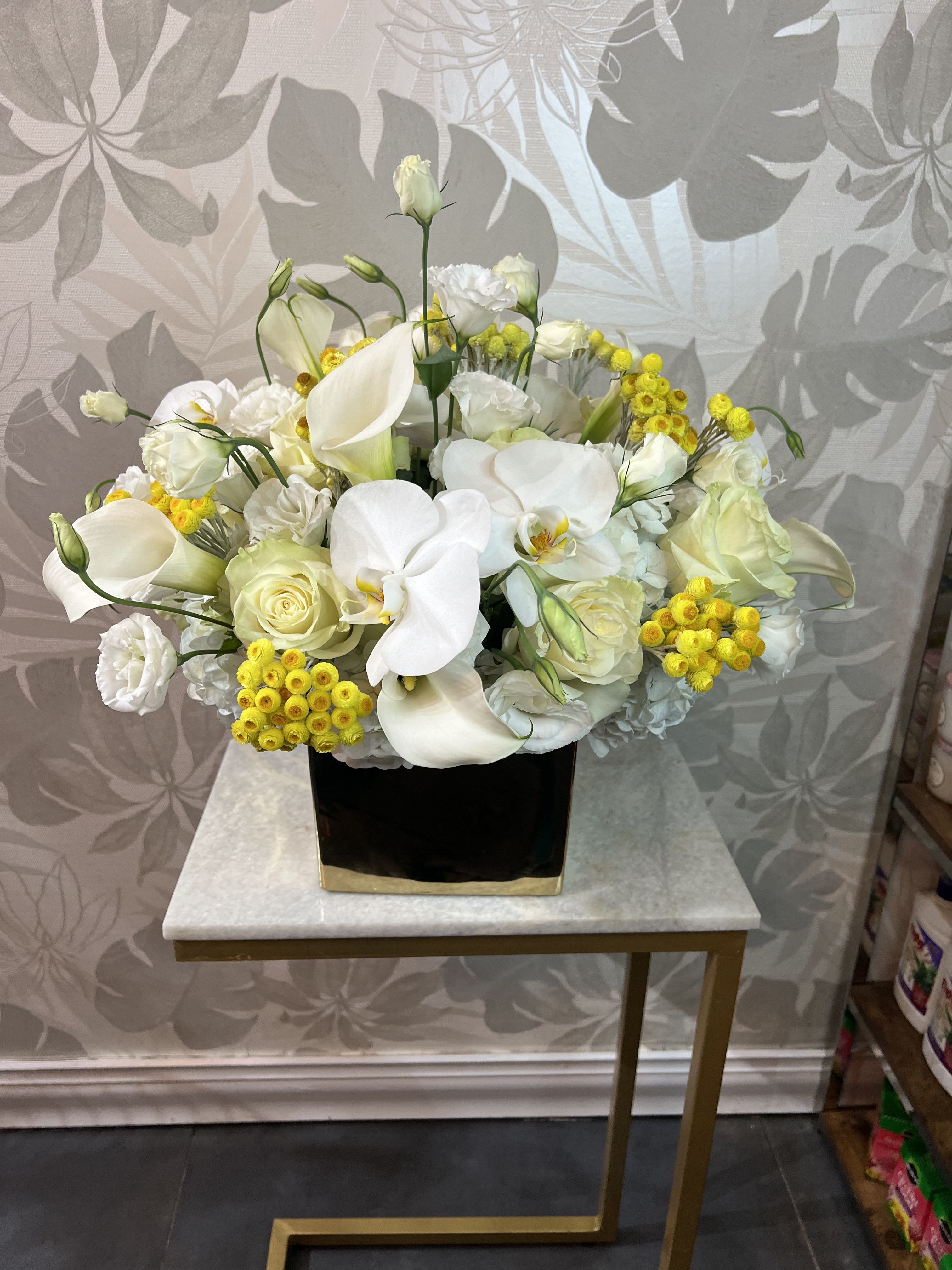 White floral arrangement with calla lilies, roses, and yellow accents in a black vase
