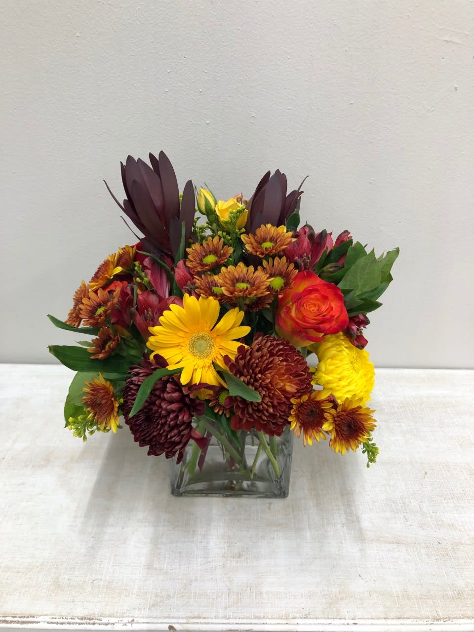 Fall In A Cube Bouquet - (PICTURES SHOWN ARE BOTH STANDARD, same arrangement)  Assortment of fall colors in a short cube vase.  Fall mums, alstromeria, roses, gerber daisies, spray roses,  safari sunset, waxflower, solidago, etc...  Flowers and colors may vary depending on availability.