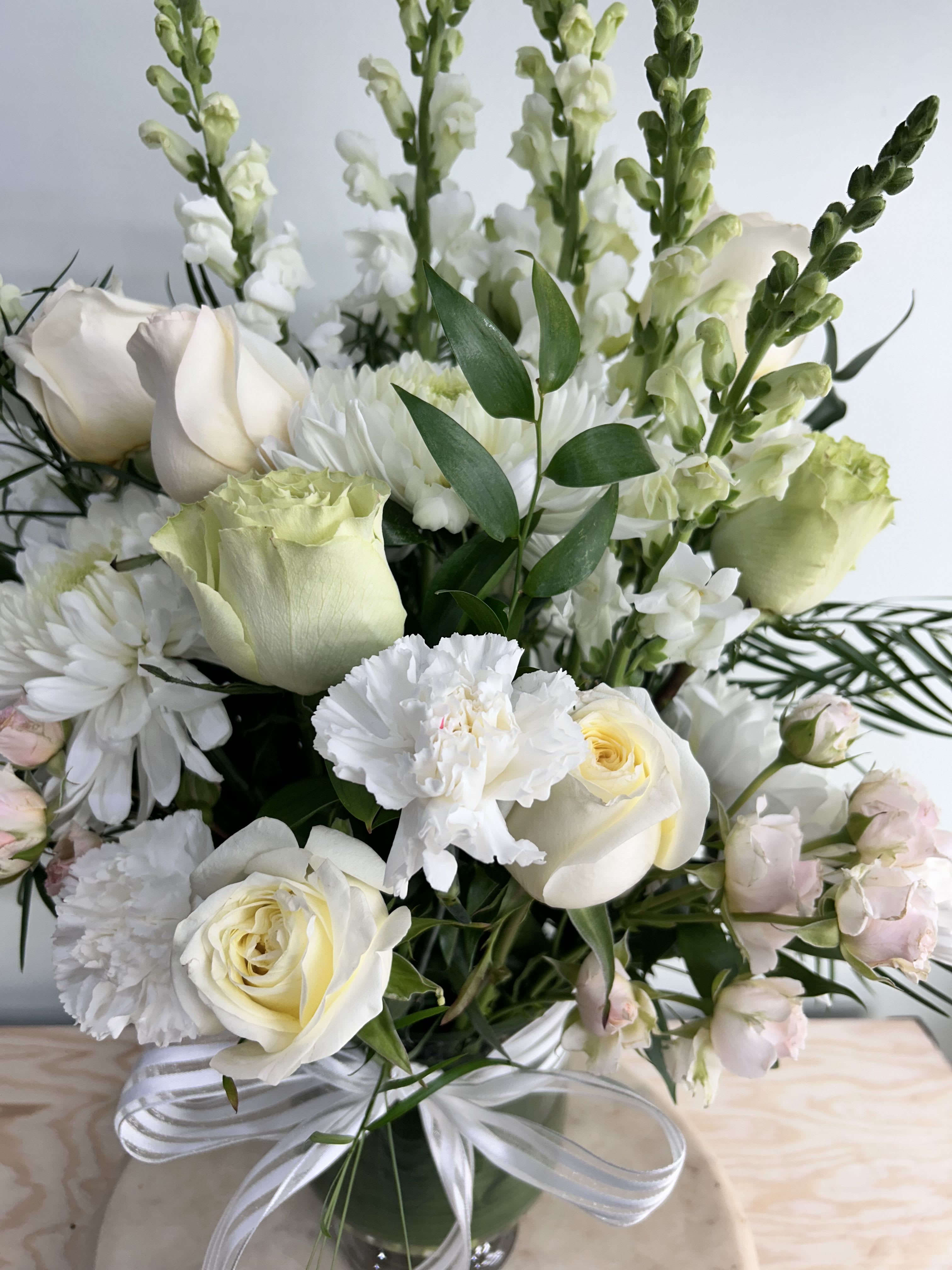 White roses and chrysanthemums in a glass vase with a ribbon